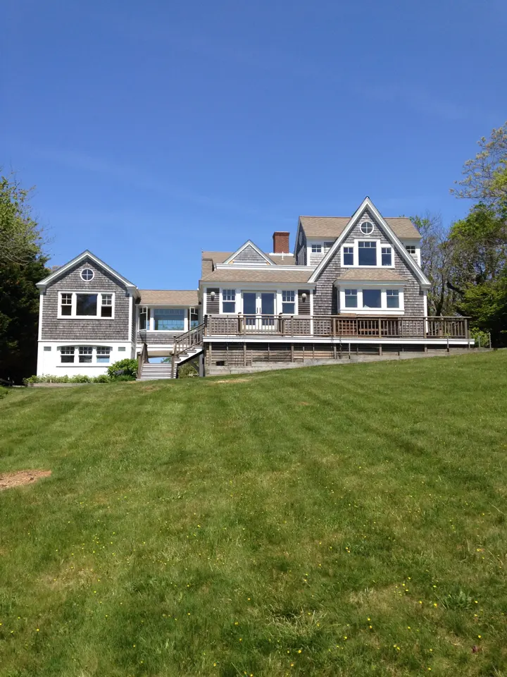 Cape Cod shingle home with a deck under a blue sky