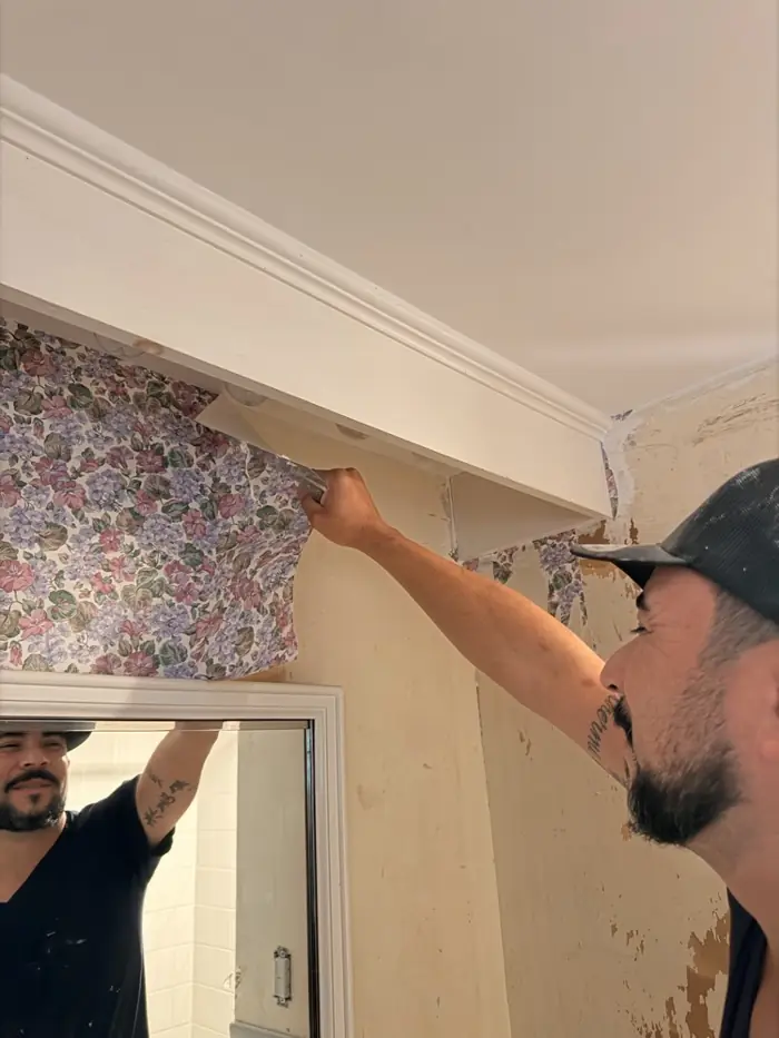Crew member removing wallpaper from a bathroom wall